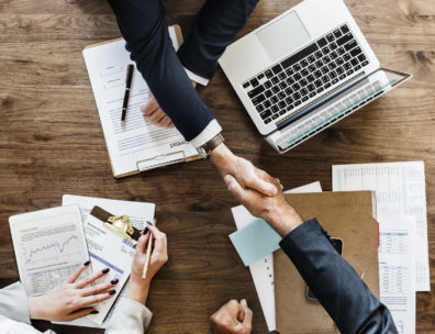 Deux professionnels se serrent la main après une prospection commerciale efficace, entourés de documents et d'un ordinateur