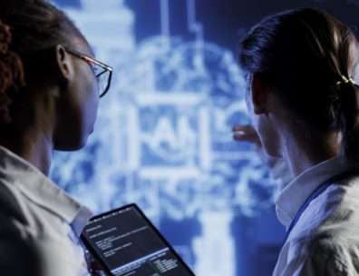 Deux professionnels analysant du code sur tablette devant un écran, en formation à l'IA générative